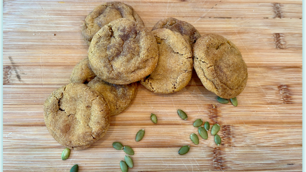 7 pumpkin snikerdoodle cookies on wood with pumpkin seeds scattered